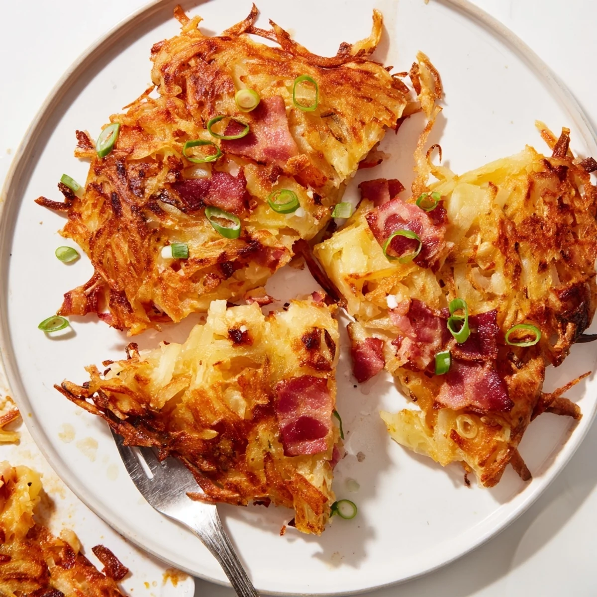 Kross gebratene Käse- und Speckkartoffelrösti, serviert mit frischen Frühlingszwiebeln.  