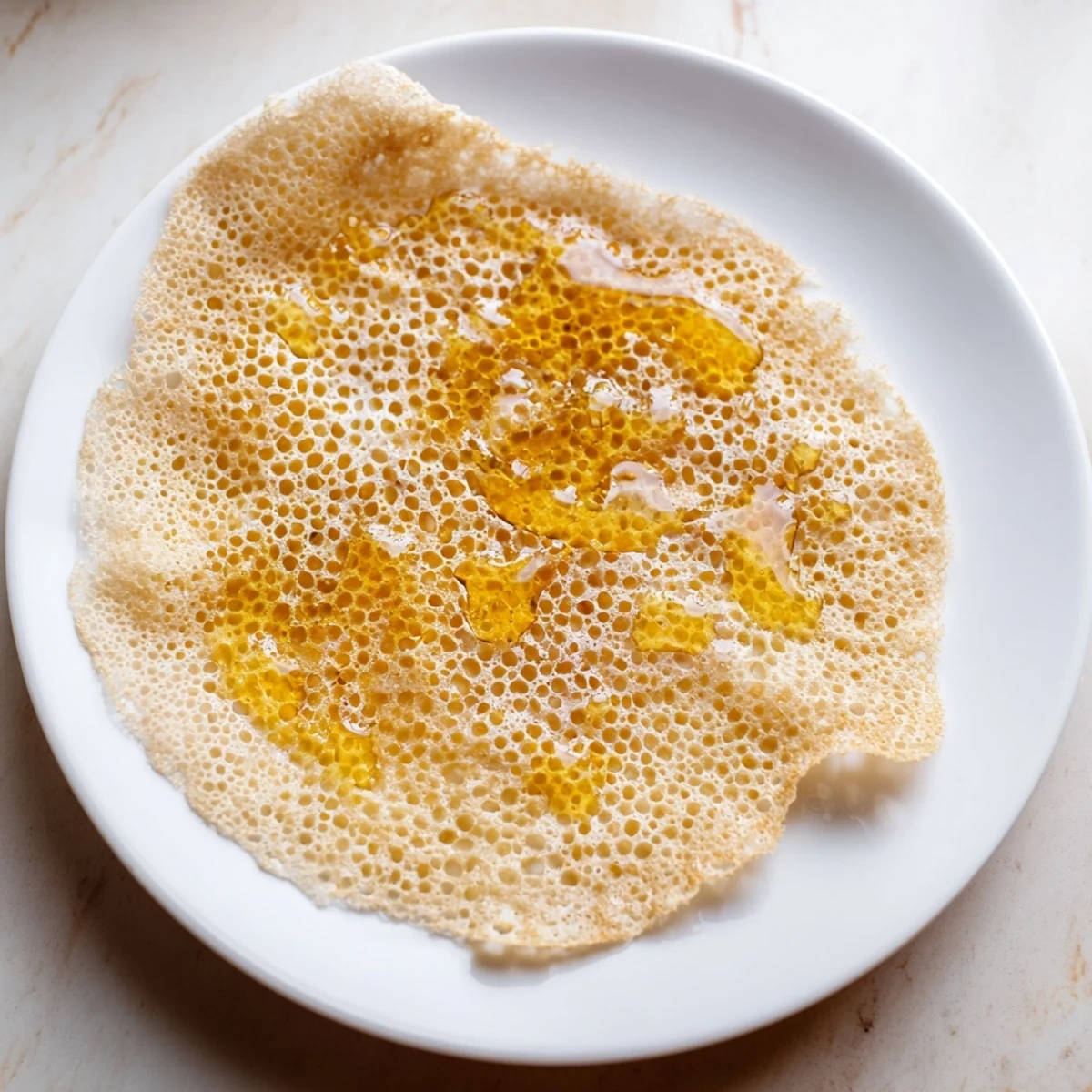 Warm, honeycomb-textured Moroccan Baghrir, served drizzled with glistening honey and melting butter.