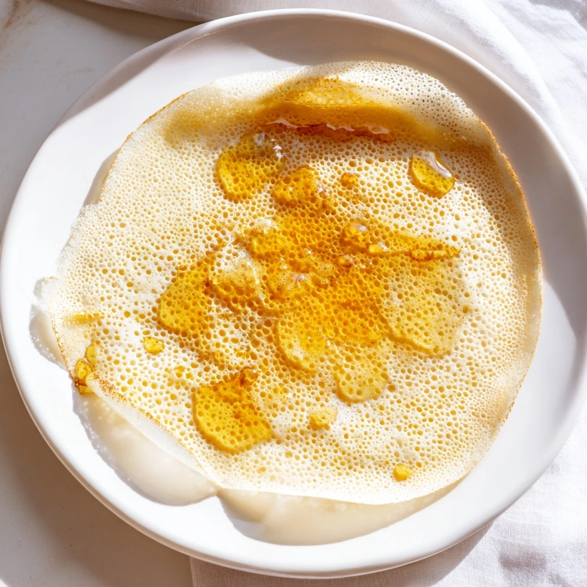 A stack of soft Moroccan Baghrir crepes, perfect for a cozy breakfast with a sweet, buttery topping.