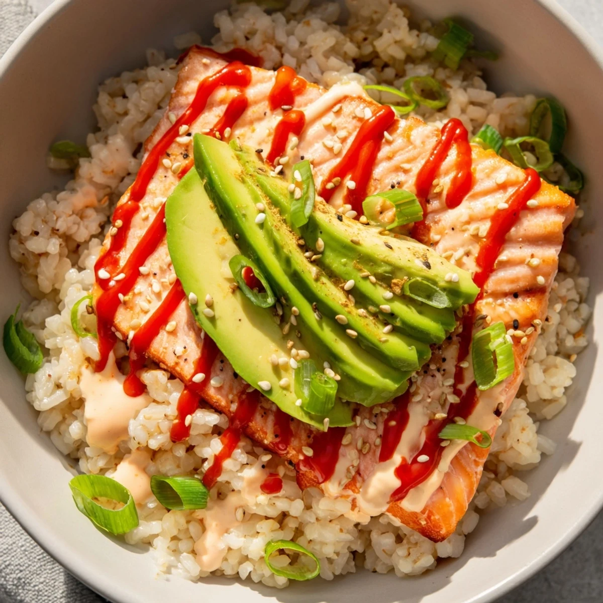 A close-up view of the easy Emily Mariko Salmon Rice Bowl, with spicy mayo and sesame seeds.