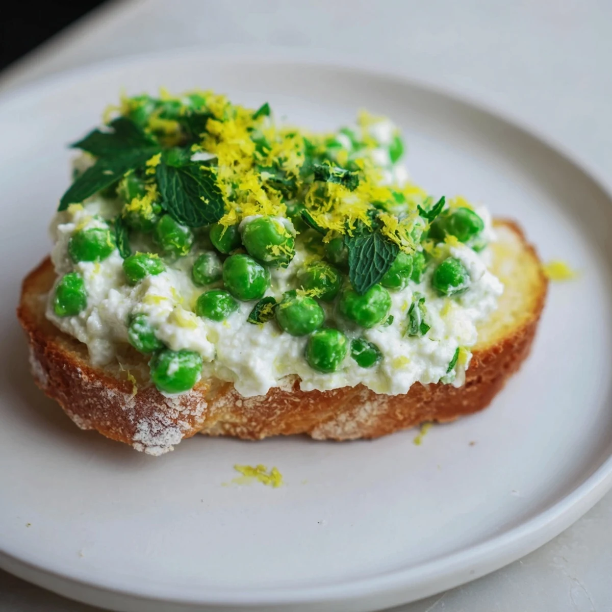 A plate of creamy pea and mint ricotta toast, topped with zesty lemon, ready to eat.