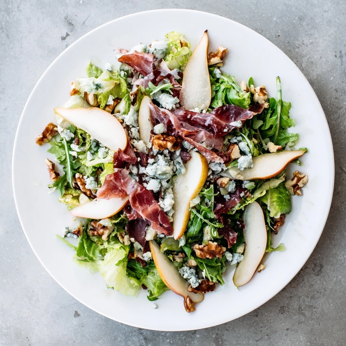 Ein leckeres Frisée, Birne, Blauschimmelkäse und knuspriger Prosciutto Salat, elegant angerichtet mit goldener Prosciutto-Brösel und frisch gehackten Walnüssen auf einer grünen Salatschüssel.