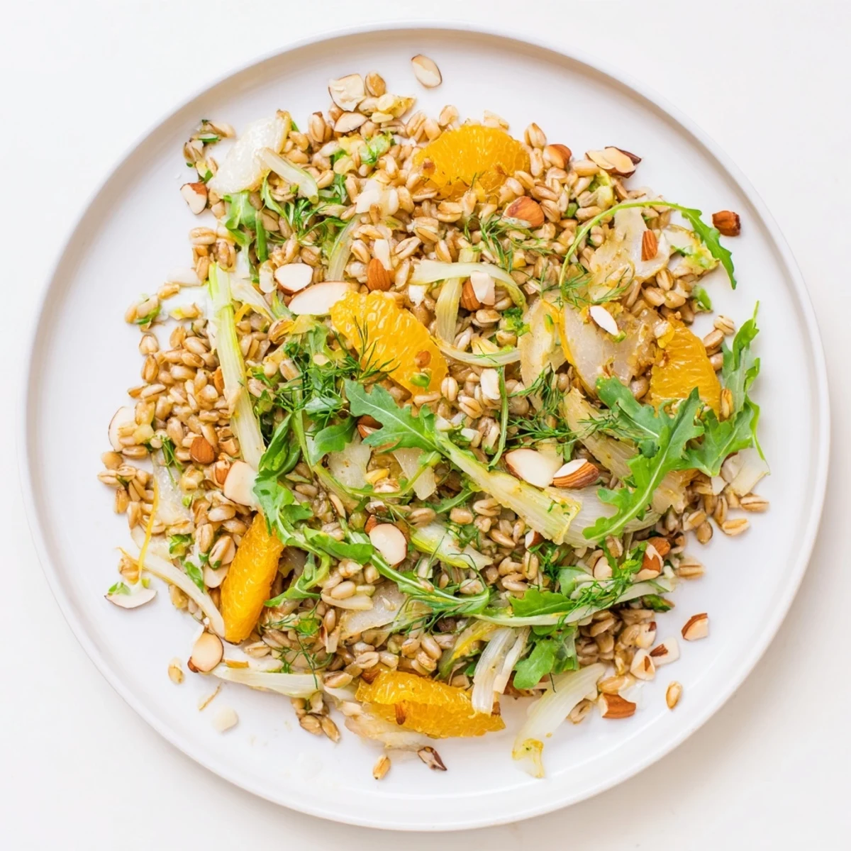 Ein farbenfrohes Farro-Salat mit Fennel, Orangen und gerösteten Mandeln auf einem rustikalen Holztisch.