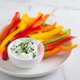 Freshly-cut bell pepper strips and herbed yogurt dip, a refreshing appetizer for everyone's enjoyment.