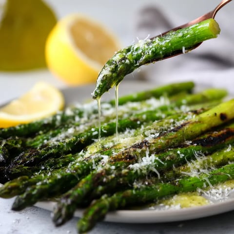 Ein weißer Teller mit grilliertem Spargel, der mit Parmesan und Zitronenvinaigrette garniert ist.