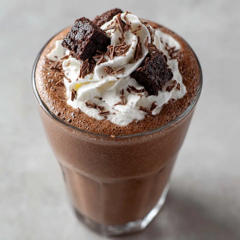 Ein Glas mit Milchshake, der mit Brownie-Streusel und -Kreuzchen garniert ist.