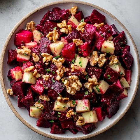 Ein Beet-Salat mit Apfel, Walnüssen und Honig-Senf-Dressing auf einem Teller.