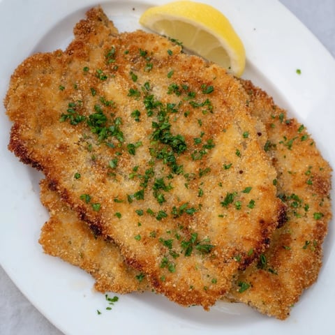 Golden-brown, crispy schnitzel-style breaded cutlets, beautifully presented with lemon wedges for serving.