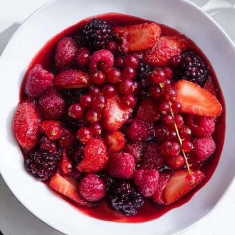 A vibrant bowl of Rote Grütze topped with creamy, rich homemade vanilla sauce.