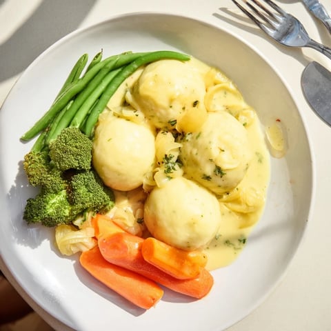 **Kartoffelklöße** floating in savory sauce, alongside colorful steamed vegetables, ready to enjoy.