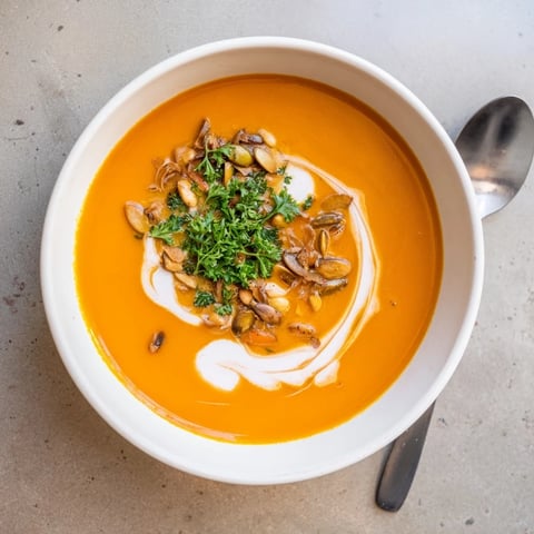 Creamy sweet potato and carrot soup ready to serve, garnished with fresh cilantro and toasted seeds.