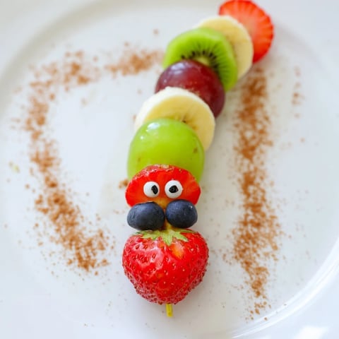 Colorful Caterpillar Fruit Skewer Track with grapes, strawberries, and a chocolate cookie crumb track.