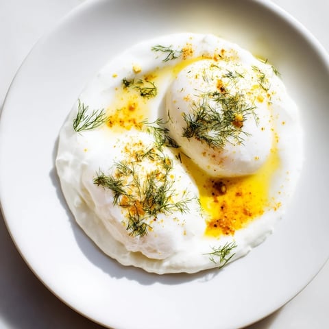 Silky poached eggs in a vibrant Cilbir dish with spiced brown butter, ready to eat.