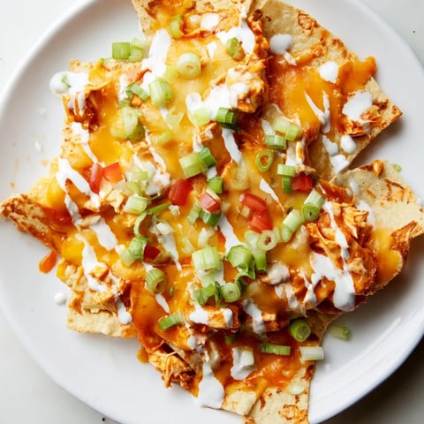 Spicy buffalo chicken nachos with melted cheese and fresh toppings, ready to eat.