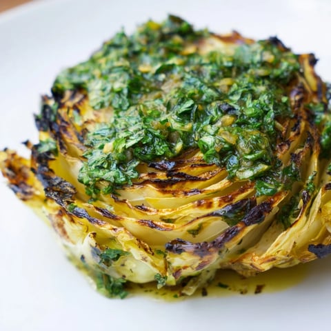 Goldbraun geröstete Cabbage Steaks mit frischer Jalapeño Chimichurri auf einem weißen Teller.