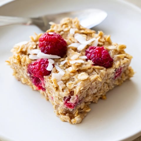 Goldene Ofenhaferflocken mit frischen Himbeeren und geröstetem Kokos auf einem Frühstückstablett, perfekt für gemütliche Morgen.