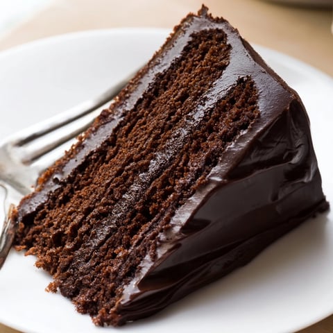 Rich slice of Easy Chocolate Fudge Cake with silky icing and fresh raspberries on a vintage plate.  