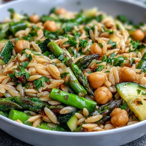 One-Pot Lemon Herb Orzo with Chickpeas and Spring Veggies in a skillet, with zucchini, asparagus, and spinach. Fresh lemon wedges and herbs garnish the easy Mediterranean dinner.