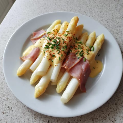 Ein weißer Teller mit Asparagus, Hollandaise und Ham.
