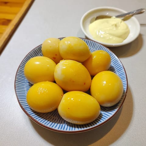 Ein weißer Teller mit einer Schüssel, die mit Mustard gefüllt ist. Darauf sind mehrere gekochte Eier, die in einem Brotaufstrich liegen.