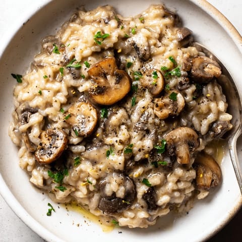 Detailaufnahme von cremigem, mit Hefeflocken verfeinertem Pilzrisotto, das mit einer Gabel servierfertig ist.