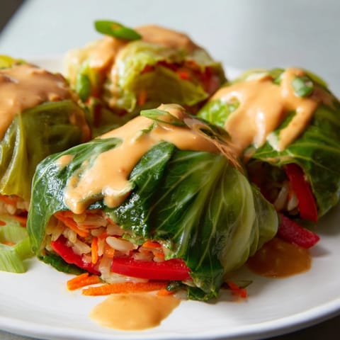 Steaming savoy cabbage rolls, filled with rice and vegetables, smothered in Thai peanut sauce.