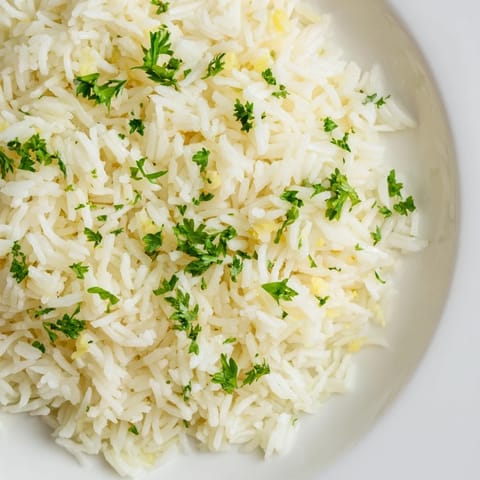 Close-up of golden-hued garlic butter rice, a flavorful side dish with fresh parsley garnish.