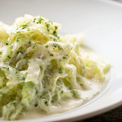 Freshly cooked Creamed cabbage steaming from a skillet, garnished with parsley and paired with crusty bread