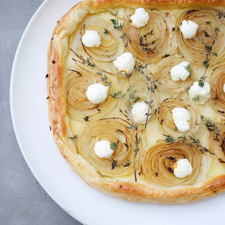 A close-up of a rustic Tarte Fine with beautifully browned onions and fresh thyme garnish.