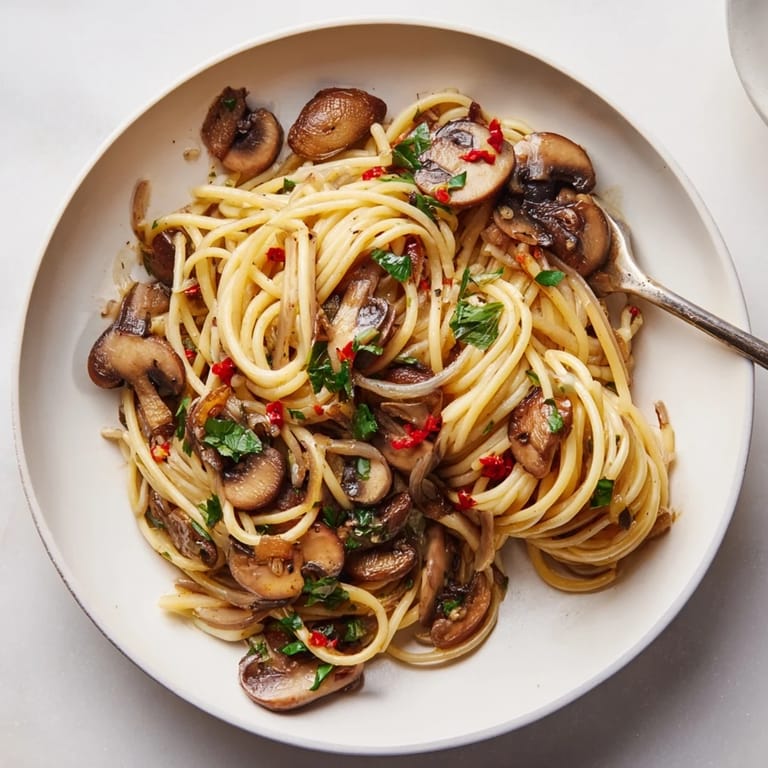 Steaming bowl of Pasta Aglio e Olio with Mushrooms, garlic, and parsley, ready to eat.