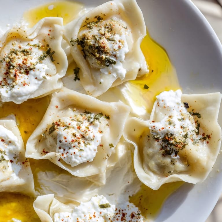 Close-up of freshly cooked Turkish Cheesy Manti; savory cheese dumplings with a vibrant, flavorful garnish.