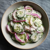 Ein weißer Teller mit einer saligen Cucumber Salat, die mit Dill und Cream garniert ist.