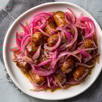 Ein weißer Teller mit sausages, die in pinken Onions eingewickelt sind, und warmem Bier.