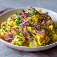 Ein weißer Teller mit Saffron Potato Salad und Pickled Onion.