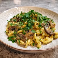 Ein weißer Teller mit Spaetzle und Mushrooms.